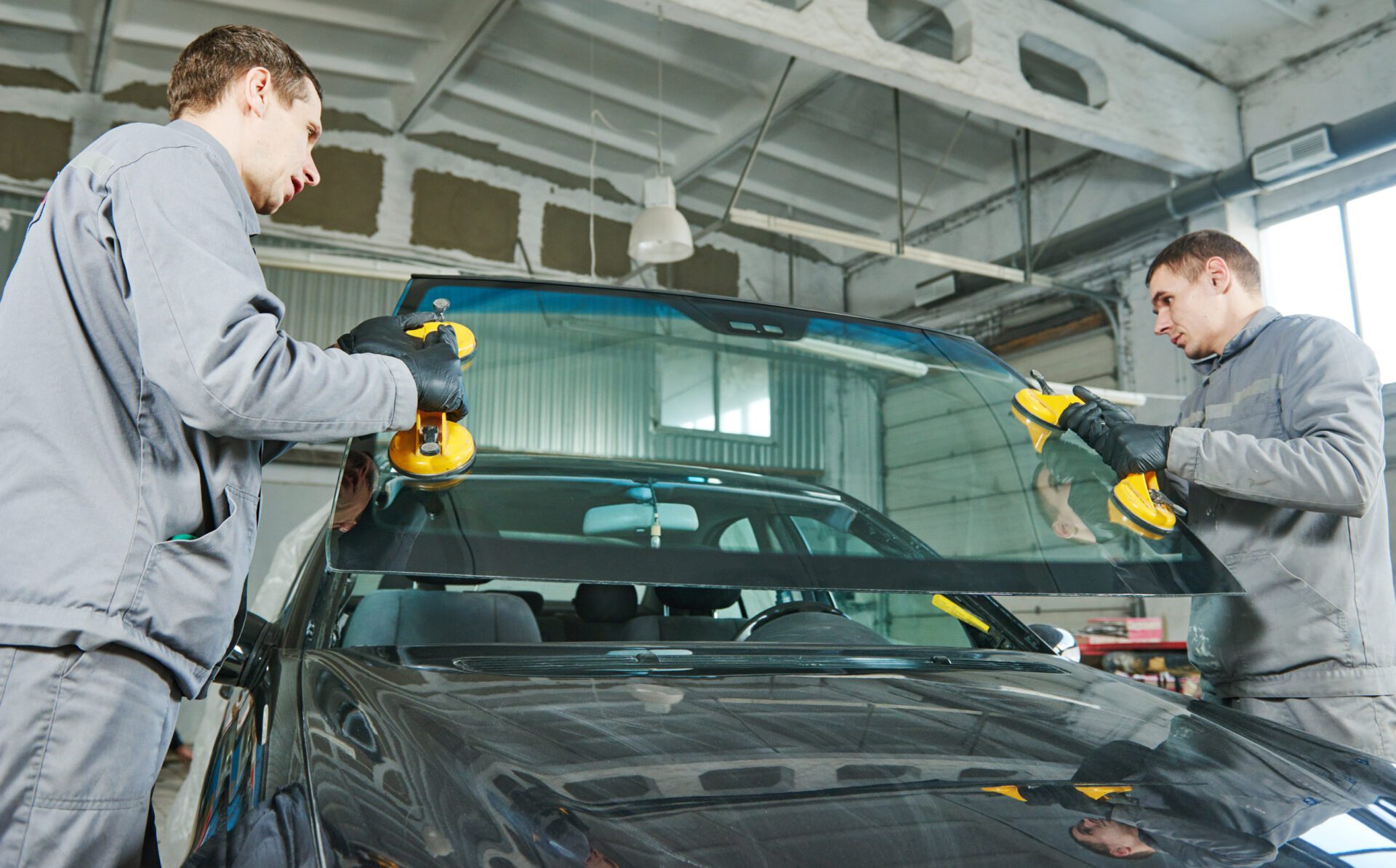 Glazier repairman mechanic worker replaces windshield or windscreen on a car in automobile workshop garage